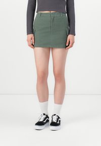 Groene denim minirok met zijzakken, hoge taille en een nette afwerking. Gekozen met zwart-witte sneakers en witte sokken.