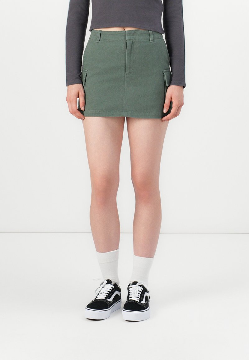 Groene denim minirok met zijzakken, hoge taille en een nette afwerking. Gekozen met zwart-witte sneakers en witte sokken.