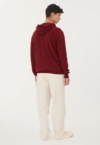 Bordeaux hoodie med dragsko i huven, bärs över krämfärgade cargobyxor. Slät struktur, avslappnad passform och inga synliga mönster eller logotyper.