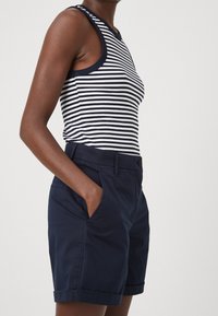 Granatowe szorty bawełniane z bocznymi kieszeniami i podwiniętymi nogawkami, w zestawieniu z bezrękawnikiem w granatowo-białe paski.