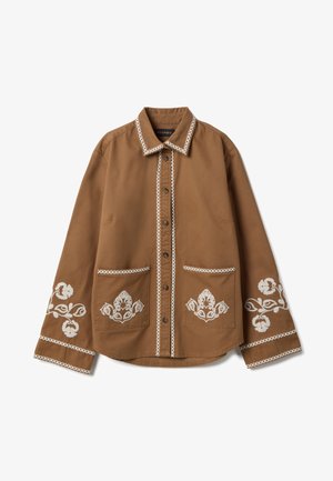 Bruin overhemd met lange mouwen en knopen, met witte geborduurde bloemmotieven op de manchetten en zakken, en witte bies langs de kraag en knopenlijst.