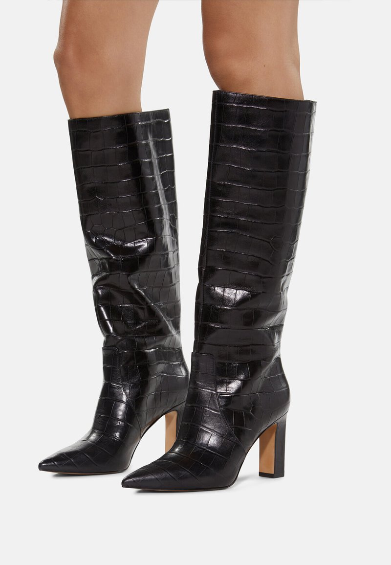 Botas negras hasta la rodilla con textura de cocodrilo brillante, punta afilada y tacones gruesos. El diseño presenta una silueta ajustada y líneas limpias.
