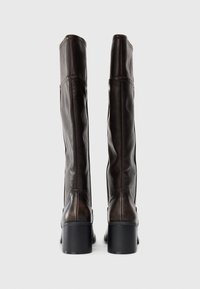 Bottes en cuir marron, jusqu'au genou, avec une texture lisse, un bout rond et un talon carré. Présente des détails de couture le long des coutures.