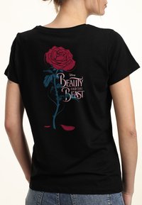 Camiseta negra con un gráfico de una rosa roja con un tallo verde azulado, acompañada por el texto "La Bella y la Bestia" en blanco y rosa.
