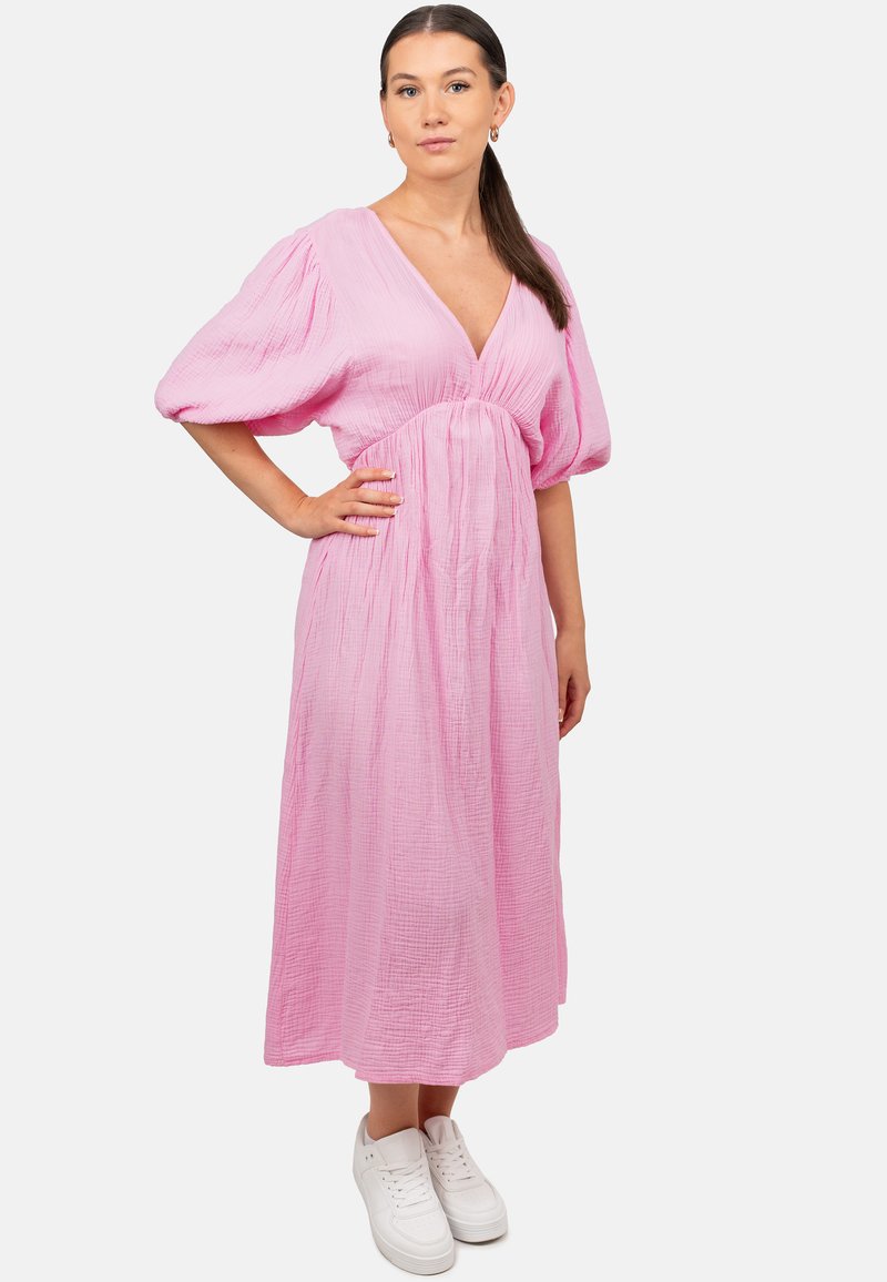 Roze midi-jurk van textuurstof met een V-hals en pofmouwen; gedragen met witte sneakers. Eenvoudige en ontspannen pasvorm.