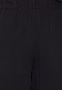 Svart tygplagg med elastisk midja och slät yta, med en avslappnad passform och subtila sömnadsdetaljer.