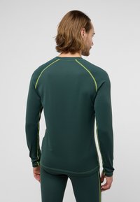 T-shirt de sport à manches longues en vert foncé avec une texture côtelée et des accents réfléchissants en jaune néon le long des coutures et du col.