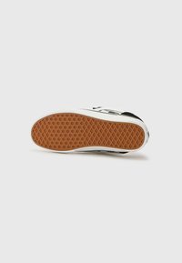 Schwarzer Sneaker mit einer strukturierten Gummisohle im Wabenmuster und einer kontrastierenden gummifarbenen Außensohle.