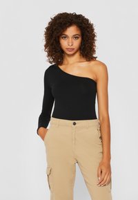 Mustapaitainen, yksi-olkapäinen bodysuit sileästä ja joustavasta kankaasta, yhdistettyinä khaki-khm pantsien kanssa, joissa on sivutaskut ja napitus.