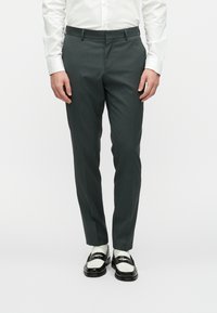 Σκουροπράσινα επαγγελματικά παντελόνια με στενή εφαρμογή, κατασκευασμένα από υφασματική ύλη με υφή. Συνδυασμένα με λευκό πουκάμισο, που αναδεικνύει έναν καθαρό, μοντέρνο σχεδιασμό.