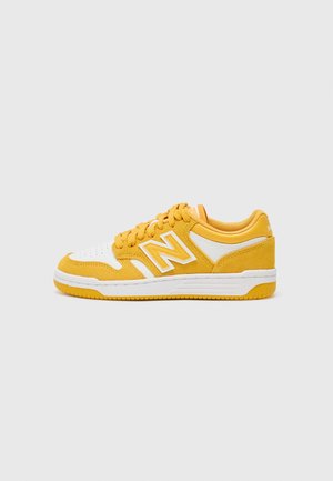 Baskets basses jaunes et blanches avec une semelle blanche et une semelle extérieure jaune, comportant des lacets jaunes et un grand logo "N" sur le côté.