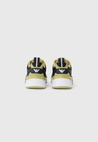 Black and olive green athletic shoes featuring a textured mesh upper, white midsole, and reflective logo detail on the heel.