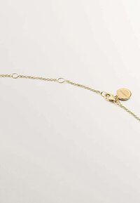 Pulsera de cadena de metal dorado con eslabones ovalados, un cierre de langosta y una etiqueta redonda. La textura suave y el acabado brillante realzan su apariencia.
