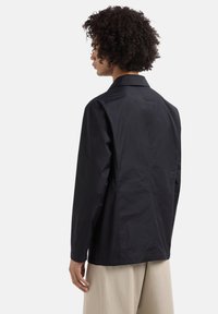 Giacca leggera nera con colletto, maniche lunghe e una finitura liscia e opaca. Il retro presenta un design pulito e affusolato.