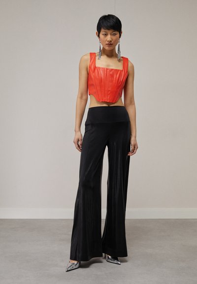 Top corto rojo con pliegues verticales, combinado con pantalones de satén negros de pierna ancha de cintura alta y tacones plateados puntiagudos. Pendientes largos metálicos.