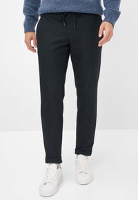 Zwarte geweven joggerbroeken met een trekkoord in de taille, slim fit en opgerolde manchetten, gecombineerd met witte sneakers. Zachte stoftextuur.