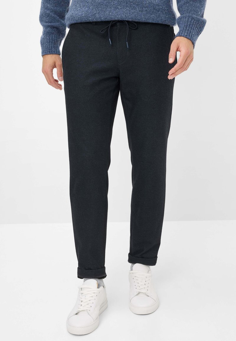 Zwarte geweven joggerbroeken met een trekkoord in de taille, slim fit en opgerolde manchetten, gecombineerd met witte sneakers. Zachte stoftextuur.