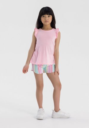 Débardeur en coton rose avec des accents en dentelle sur les épaules et un short à rayures multicolores. Le mannequin porte des baskets blanches et se tient sur un fond uni.