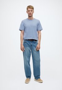 Šviesiai mėlyna trumpomis rankovėmis marškinėliai su apskritu kaklu, derinami su laisvo kirpimo šviesiai mėlynais džinsais ir kreminės spalvos sportbačiais. Paprastas dizainas, minimalūs detalės.