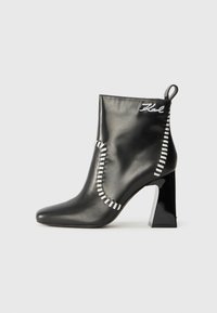 Bottine en cuir noir avec un bout pointu, un talon carré, des détails de couture blanche et une poignée en boucle à l'arrière.