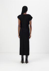 Black maxi dress with short sleeves, fitted bodice, and a smooth texture. Worn with knee-high, shiny black heeled boots.