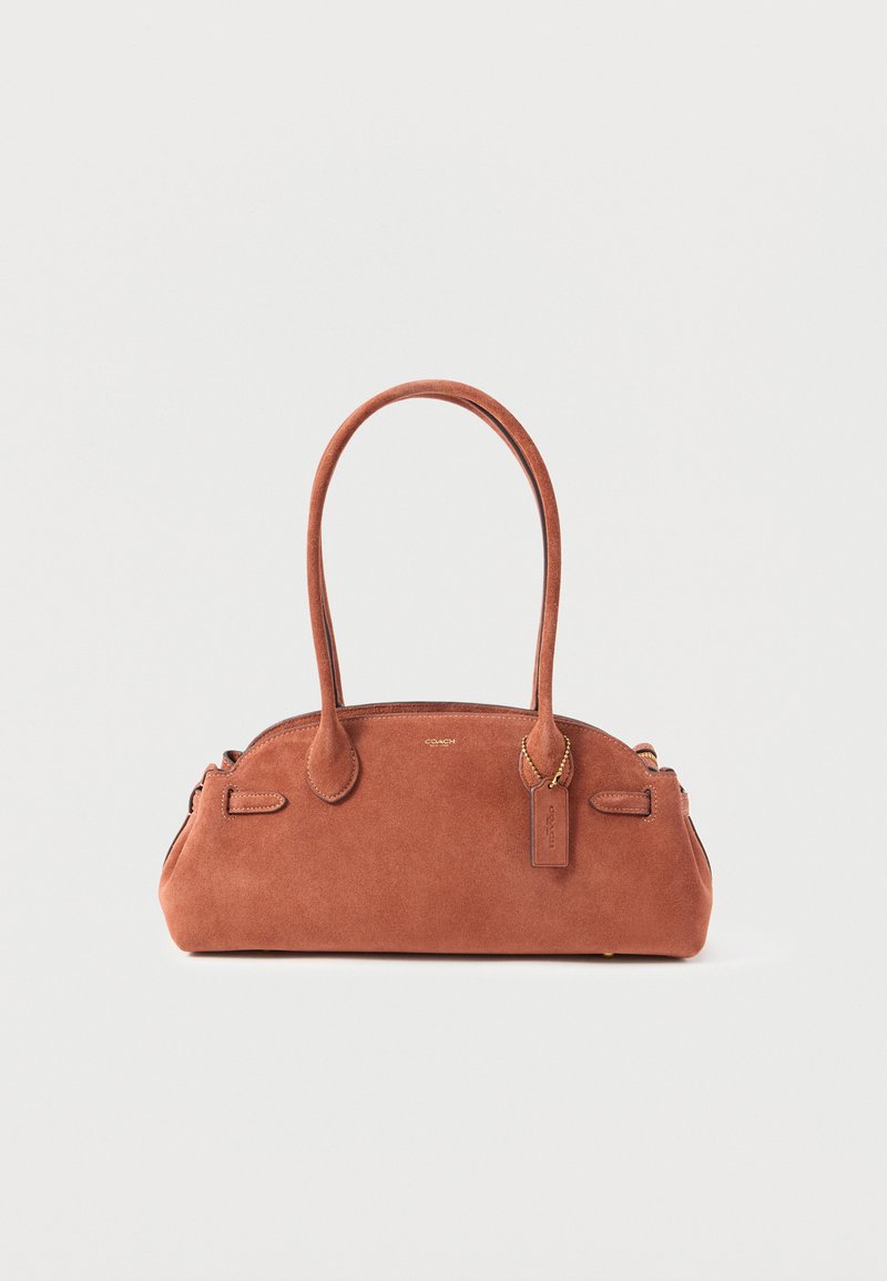 Μικρή καφέ τσάντα από καστόρι με διπλούς ιμάντες ώμου και ταμπελάκι με το λογότυπο της Coach που κρέμεται κοντά στη λαβή.