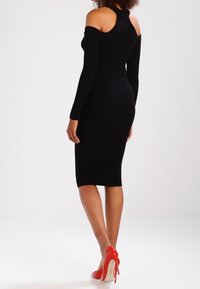 Abito nero in maglia a spalle scoperte con maniche lunghe e silhouette aderente. Abbinato a scarpe con tacco rosse.