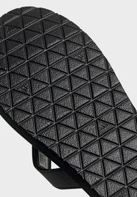 Suela de chancla de goma negra con un diseño de textura en forma de diamante, con detalles de logotipo en relieve y un borde suave.