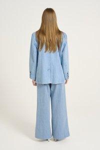 Blazer en denim bleu clair et pantalon à jambes larges, avec une coupe décontractée, un tissu texturé et des accents de boutons sur les manches. Vue de dos affichée.