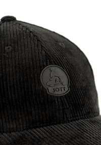Black corduroy cap featuring vertical ribbed texture, round JOTT logo patch in matte black, and a curved brim.