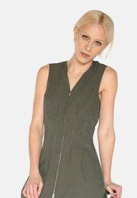 Ärmelloses, olivgrünes Kleid mit Reißverschluss vorne, das vertikale Nähte und ein figurbetontes Design aufweist, gefertigt aus einem leichten Stoff.