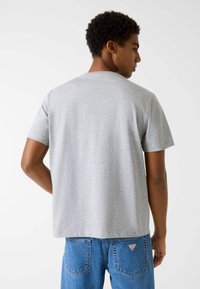 Szara bawełniana koszulka z krótkimi rękawami, o luźnym kroju i okrągłym dekolcie. Widok z tyłu ukazuje gładką teksturę, brak grafik oraz subtelny brzeg.