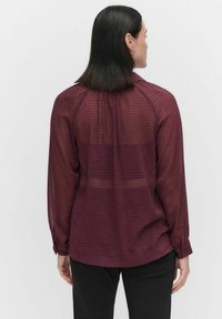 Maroon blouse met een textuurpatroon, lange mouwen en verstelbare manchetten, met een ontspannen pasvorm en licht doorschijnende stof.