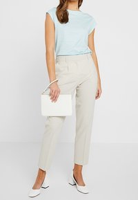 Lichtblauwe gestreepte short-sleeve top, beige op maat gemaakte broek, witte block-heeled schoenen en een witte rechthoekige handtas.