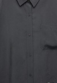 Chemise gris foncé à boutons avec col pointu et poche poitrine sur une surface plane.