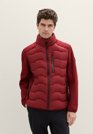 Rote gepolsterte Jacke mit hohem Kragen, mit einem Zickzack-Steppmuster und seitlichen Reißverschlusstaschen. Glattes Material mit kontrastierenden texturierten Ärmeln.
