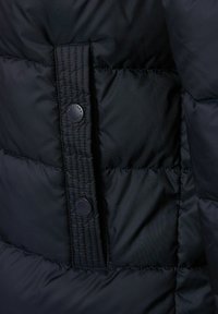 Czarna kurtka puchowa o pikowanej fakturze, z zapięciem na guziki. Materiał wydaje się gładki i lekko błyszczący.