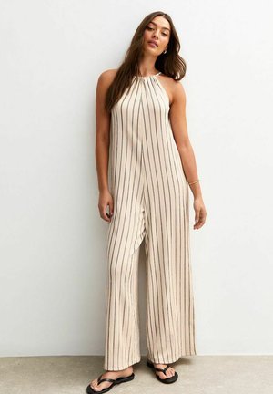 Beige stripad jumpsuit med halterneck-design, vida ben och en löst sittande passform, tillverkad av ett lättviktsmaterial. Svart sandaler kompletterar outfiten.