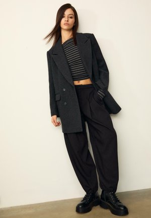 Un blazer oversize nero, un crop top a righe e pantaloni neri larghi. Stivali chunky neri con lacci. Tessuto morbido, design minimalista e vestibilità sartoriale.