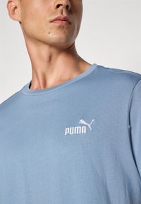 Světle modré bavlněné tričko s kulatým výstřihem a vyšitým bílým logem Puma na hrudi. Měkká textura a pohodlný střih.