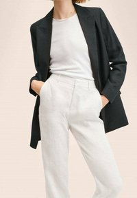 Černý blazer přes bílou košili, doplněný světle zbarvenými strukturovanými kalhotami. Oblečení má klasický design a dobře padnoucí střih.