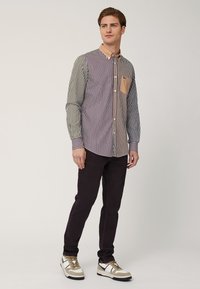 Camicia a righe con colletto e taschino a contrasto, caratterizzata da linee verticali in colori scuri e chiari. Abbinata a pantaloni scuri e sneakers.