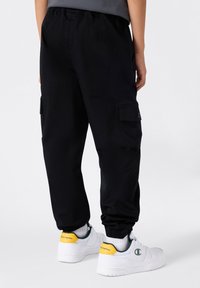 Pantaloni cargo neri con polsini elasticizzati, dotati di tasche laterali e dalla vestibilità comoda. Abbinati a sneakers bianche e una maglietta grigia.