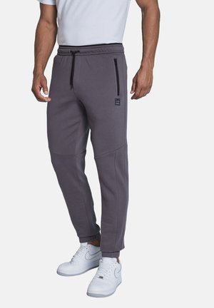 Gray jogger pants with a drawstring waist, side zipper pockets, tapered legs, and ribbed cuffs. Paired with white sneakers.