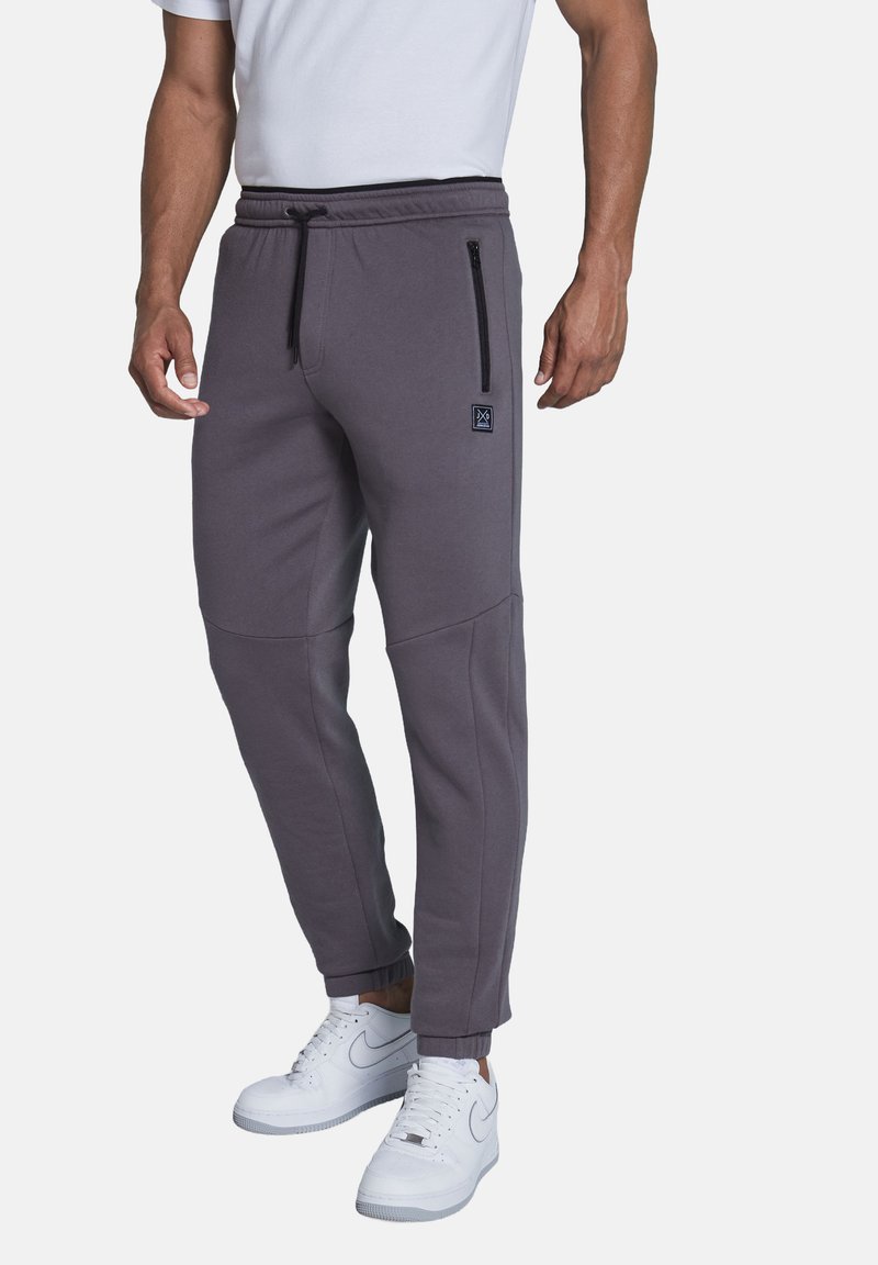Gray jogger pants with a drawstring waist, side zipper pockets, tapered legs, and ribbed cuffs. Paired with white sneakers.