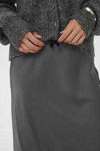 Gilet en tricot gris avec des poignets côtelés, superposé à une jupe en satin gris foncé lisse dotée d'un cordon de serrage avec un nœud noir.