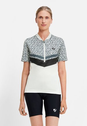 Woman in a short-sleeve cycling jersey with leopard print and black cycling shorts standing against a plain background.