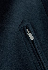 Dunkelblauer Fleece-Stoff mit einer eingenähten Tasche und einem silbernen Reißverschluss, glatter Textur und minimalen Nähten.