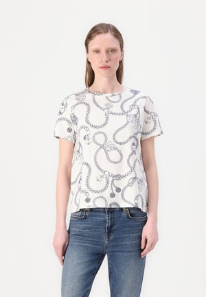 White short-sleeved t-shirt with a blue abstract rope pattern. Round neckline and relaxed fit. Paired with blue denim jeans.