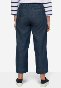 Mörkblå denimculotter med elastisk midja, bakfickor och uppvikta fållar, i kombination med mörka skor mot en vit bakgrund.